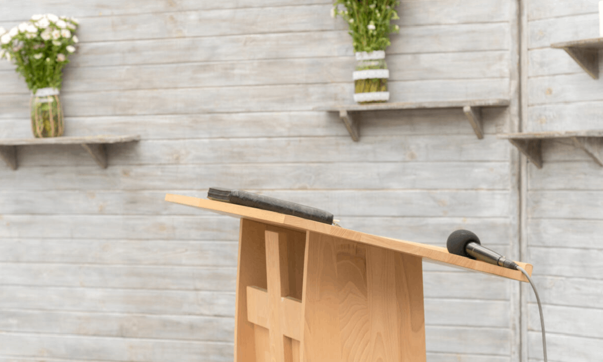 Choosing an Officiant for the Funeral Service A wooden lectern with a microphone and book, set against a light timber wall with floral arrangements.