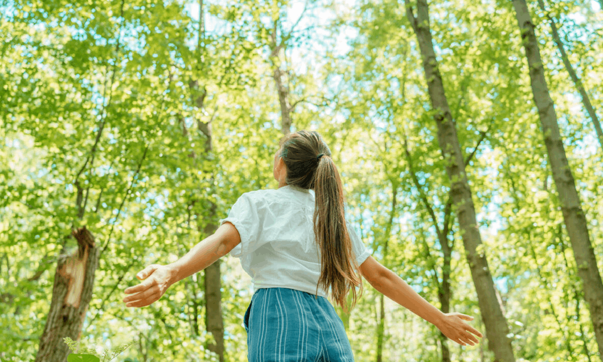 No Funeral Service Cremation: A Simplified and Private Farewell A woman standing in a sunlit forest with her arms outstretched, surrounded by tall green trees.