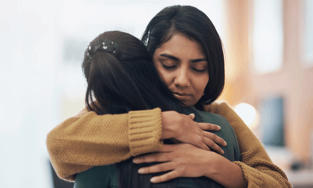Two people embracing, with one woman comforting the other in a supportive hug.